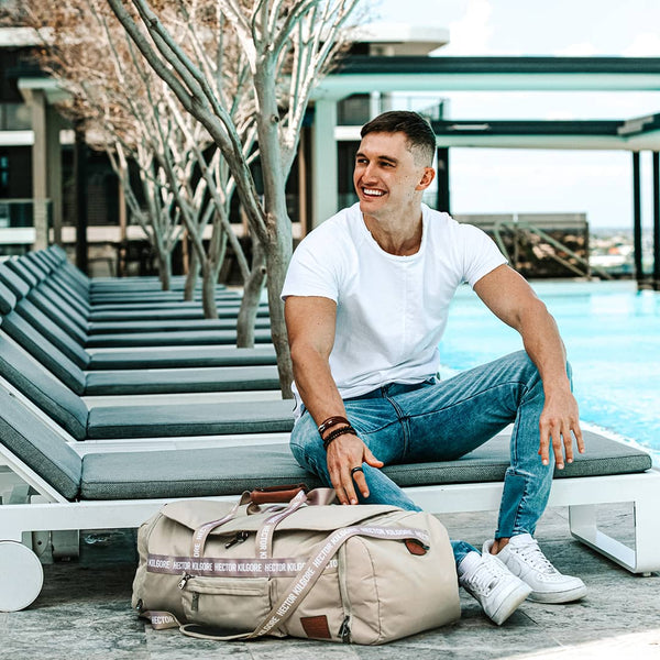Man sitting by the pool with cream beige duffle travel bag